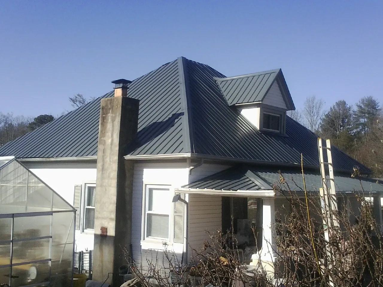 Dark blue standing seam metal roof on a white farmhouse with dormer — Slate & Tile Roof Repair by Roofing Brothers in Howard