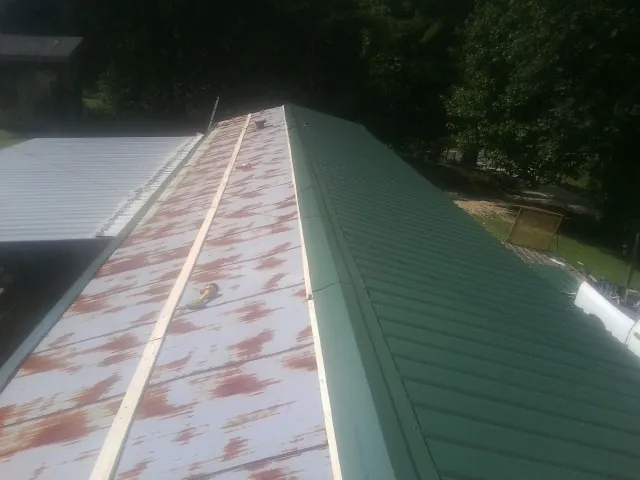 Old rusted panels beside newly installed green metal roofing — Wind Damage Roof Repair by Roofing Brothers in Howard
